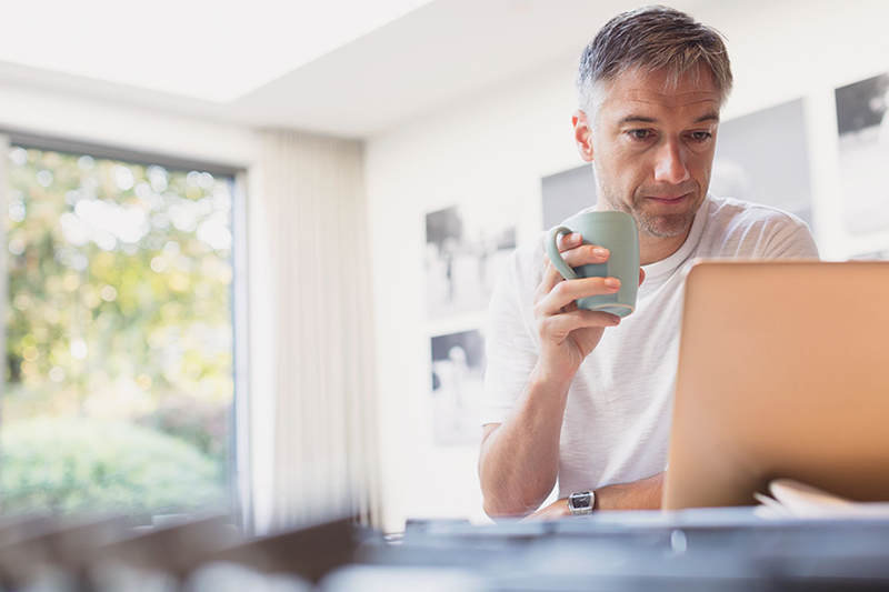 Client reviewing retirement plan on laptop while holding a cup of coffee.