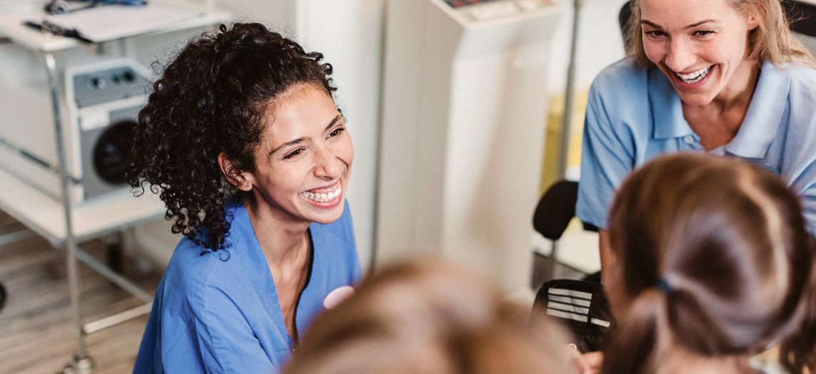 A nurse smiling as she’s talking with a little girl and her mother