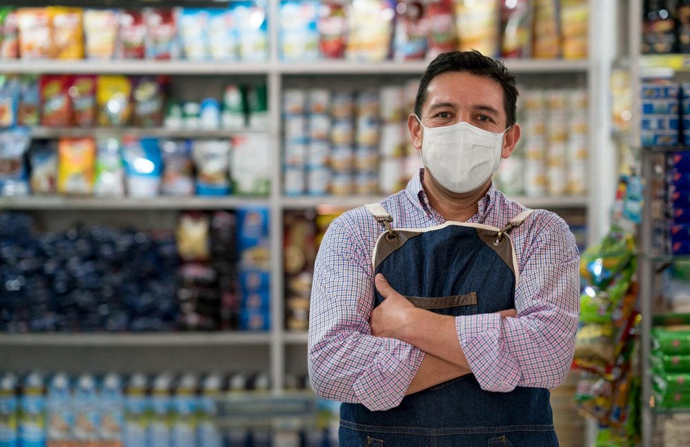 Business owner working at a grocery store wearing a facemask to mitigate COVID impacts.