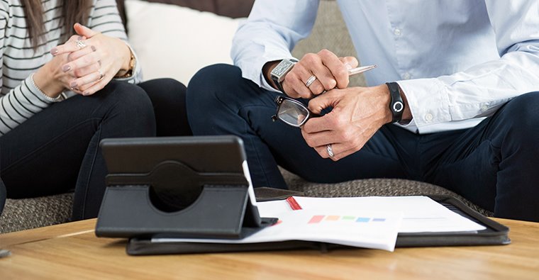 Financial advisor talking with client with paperwork and tablet on table.