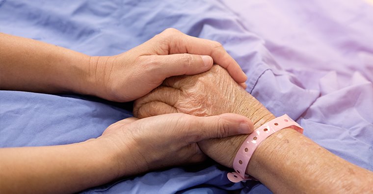 young adult hands holding on to elderly hand in hospital.