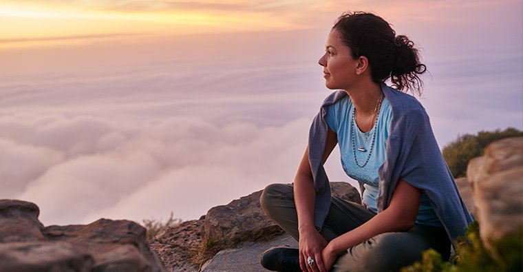 Woman reflecting on a hike, looking out to the sky.