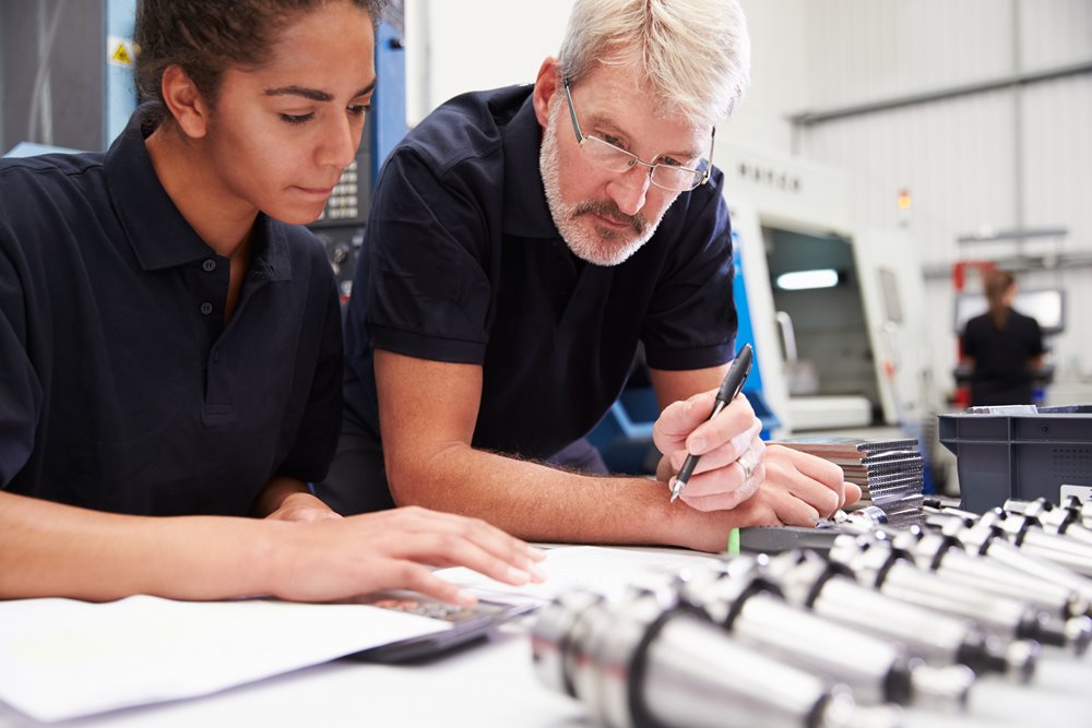 Male and female cowowrkers calculating engineering plans at a desk together.