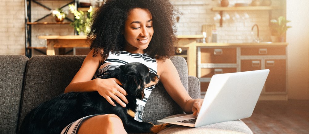 Young woman sitting on couch with dog while logging into her retirement account.