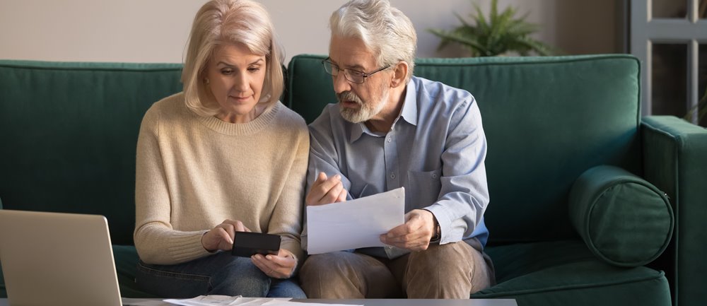 Older couple sit on couch while reviewing retirement investment statements and instructions.