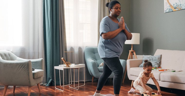 Woman practicing yoga in living room with child playing at side.