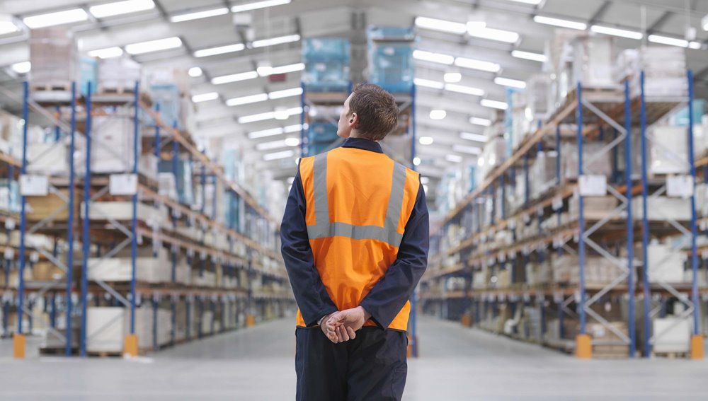 Male warehouse employee looking up at products on the stocked shelves.